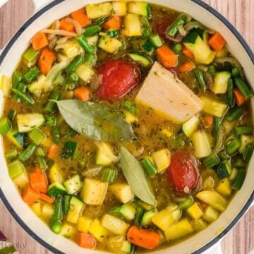 Broth, tomato paste, parmesan rinds and bay leaves added to the vegetables in a stock pot.