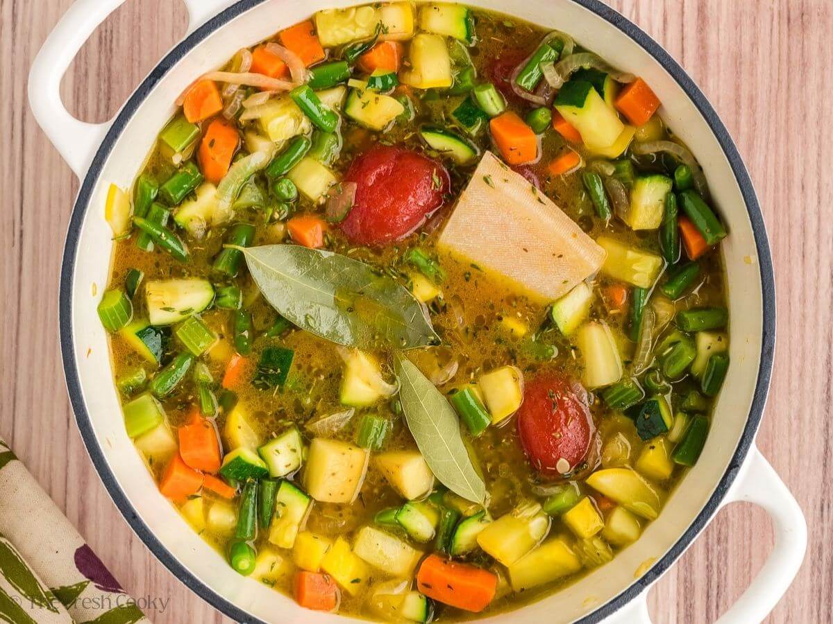 Broth, tomato paste, parmesan rinds and bay leaves added to the vegetables in a stock pot.