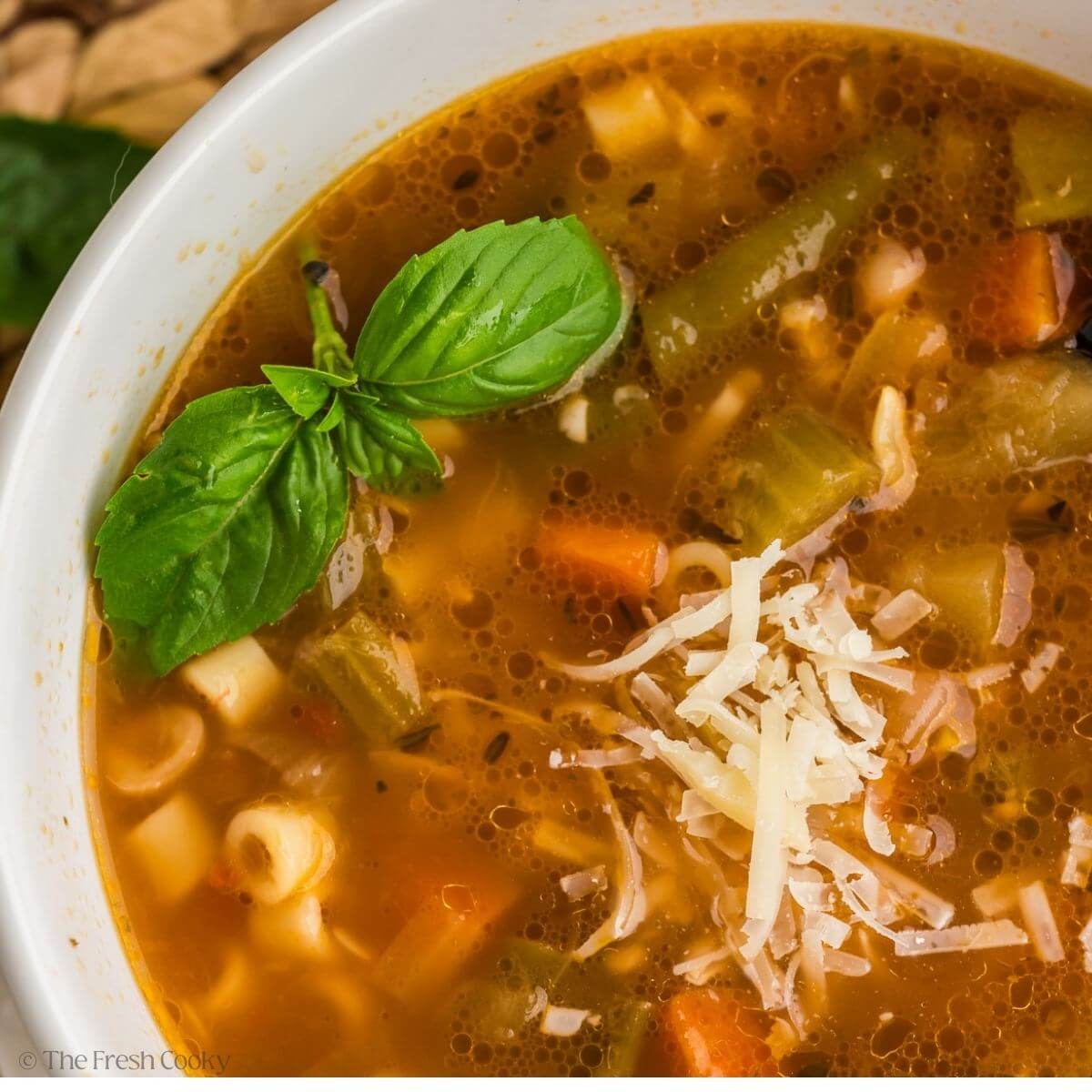 Overhead shot of a bowl of minestrone soup topped with Parmesan and basil leaves.