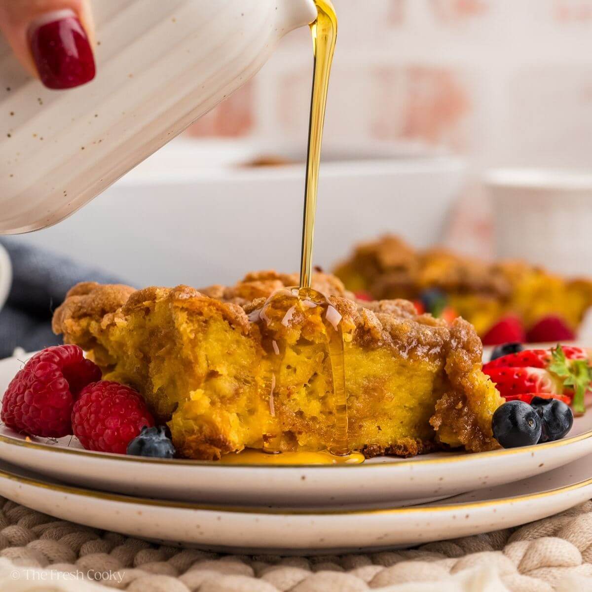 Slice of Cinnamon crunch French toast on a plate with a hand pouring maple syrup.