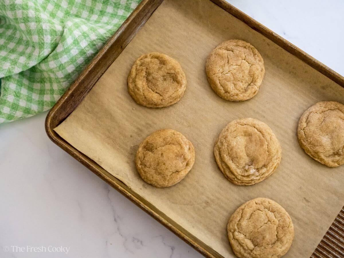 Snickerdoodle cookies on a sheet pan lined with parchment paper after being baked.