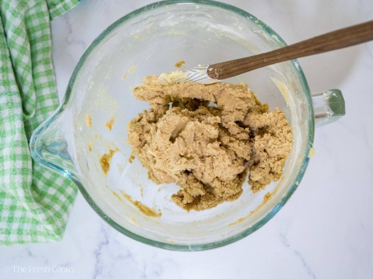 Snickerdoodle cookie dough in a glass stand mixer bowl and a rubber spatula.