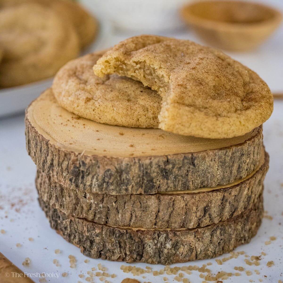 Two snickerdoodle cookies on top of a stack of wooden coasters with one cookie missing a bite.