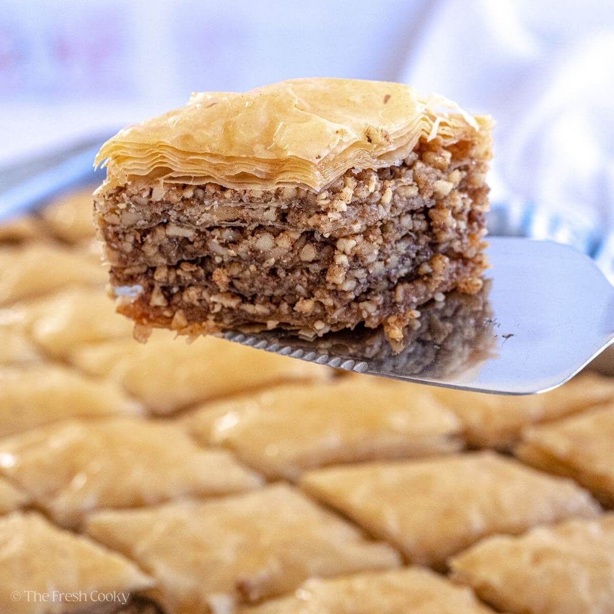 Metal spatula holding a slice of baklava over the baking dish of the rest of the baklava.