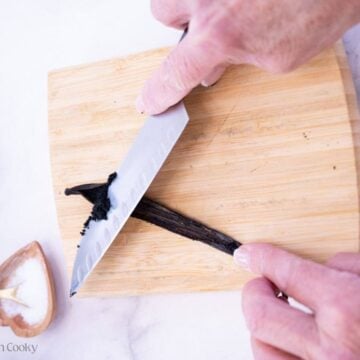 Two hands using a knife to push out the vanilla from a pod.