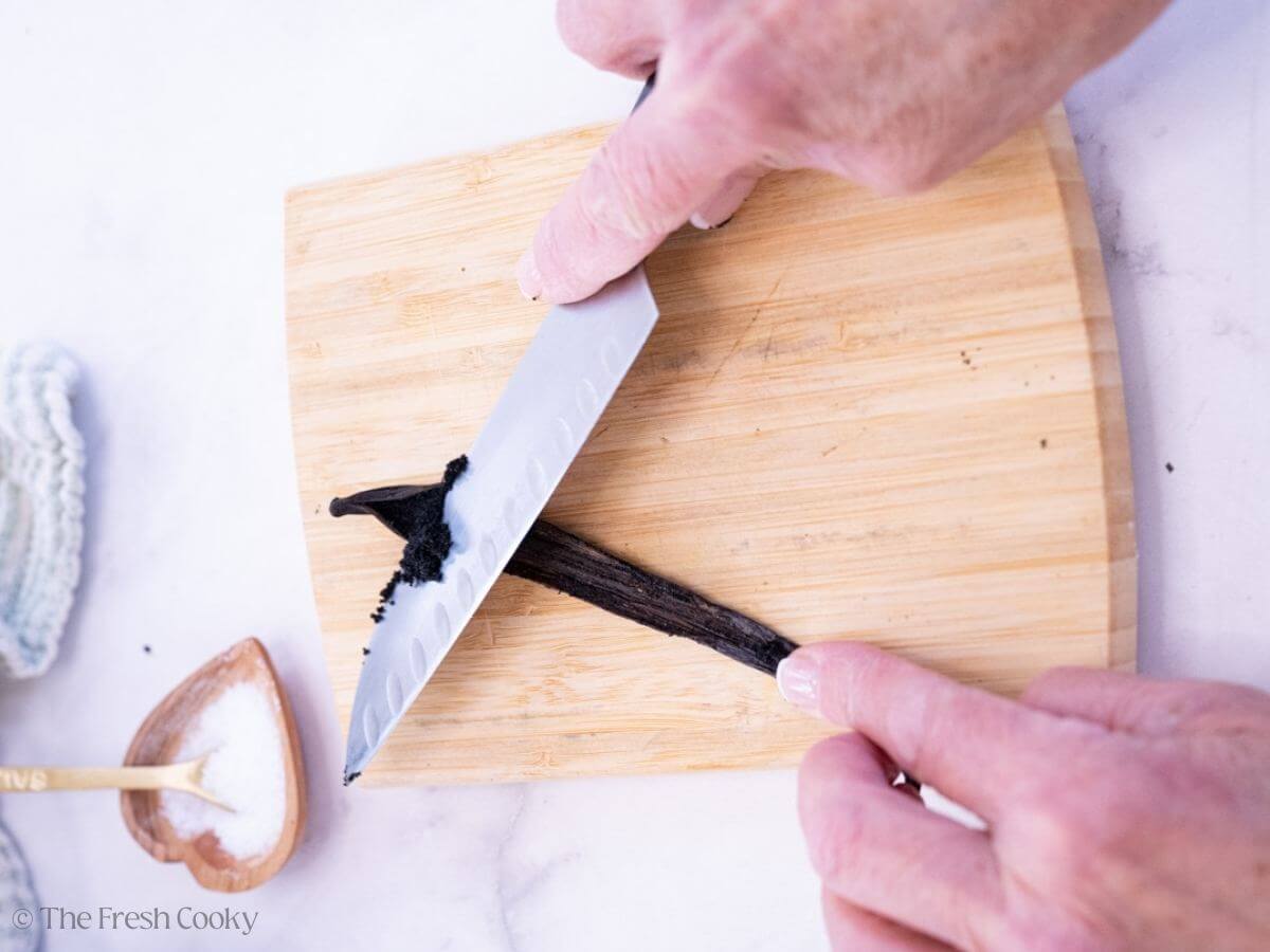 Two hands using a knife to push out the vanilla from a pod.