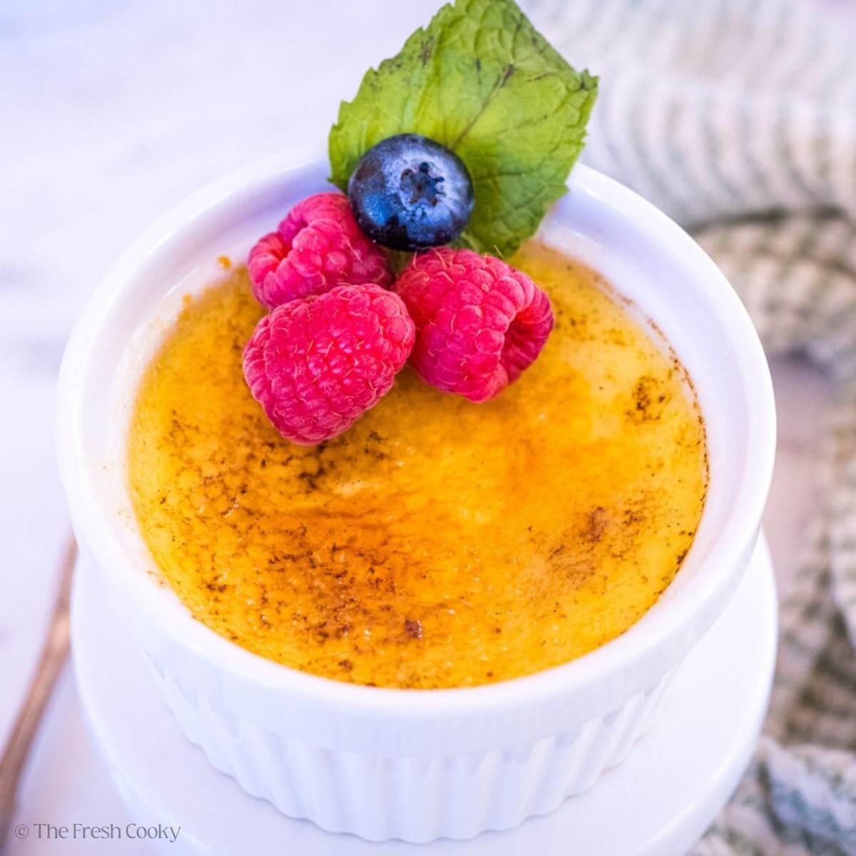 Creme brulee in a small white ramekin, garnished with berries and a mint leaf.