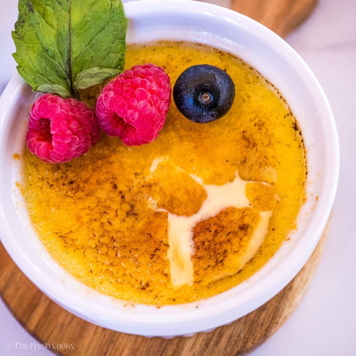 Crack sugar crust on a creme brulee topped with fresh raspberries and blueberry and mint sprig.