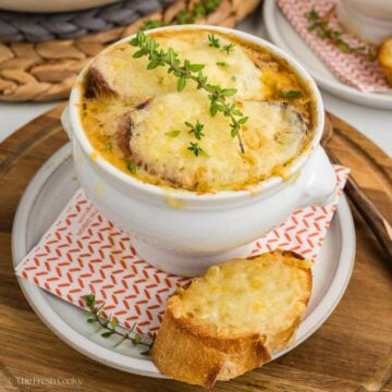 Soup cup of french onion soup with a cheese layer on top and fresh thyme.