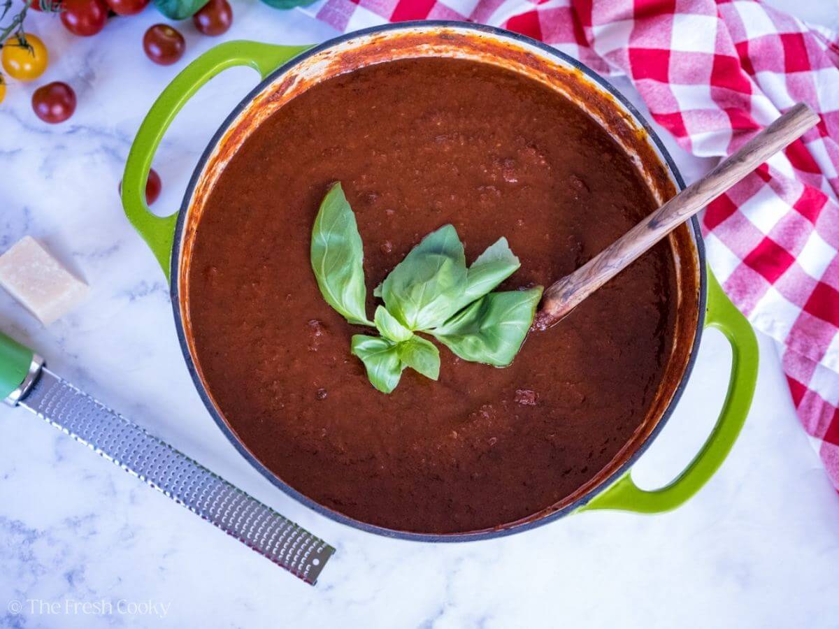 Looking down at a pot of rich, thick pasta sauce with fresh basil on top.