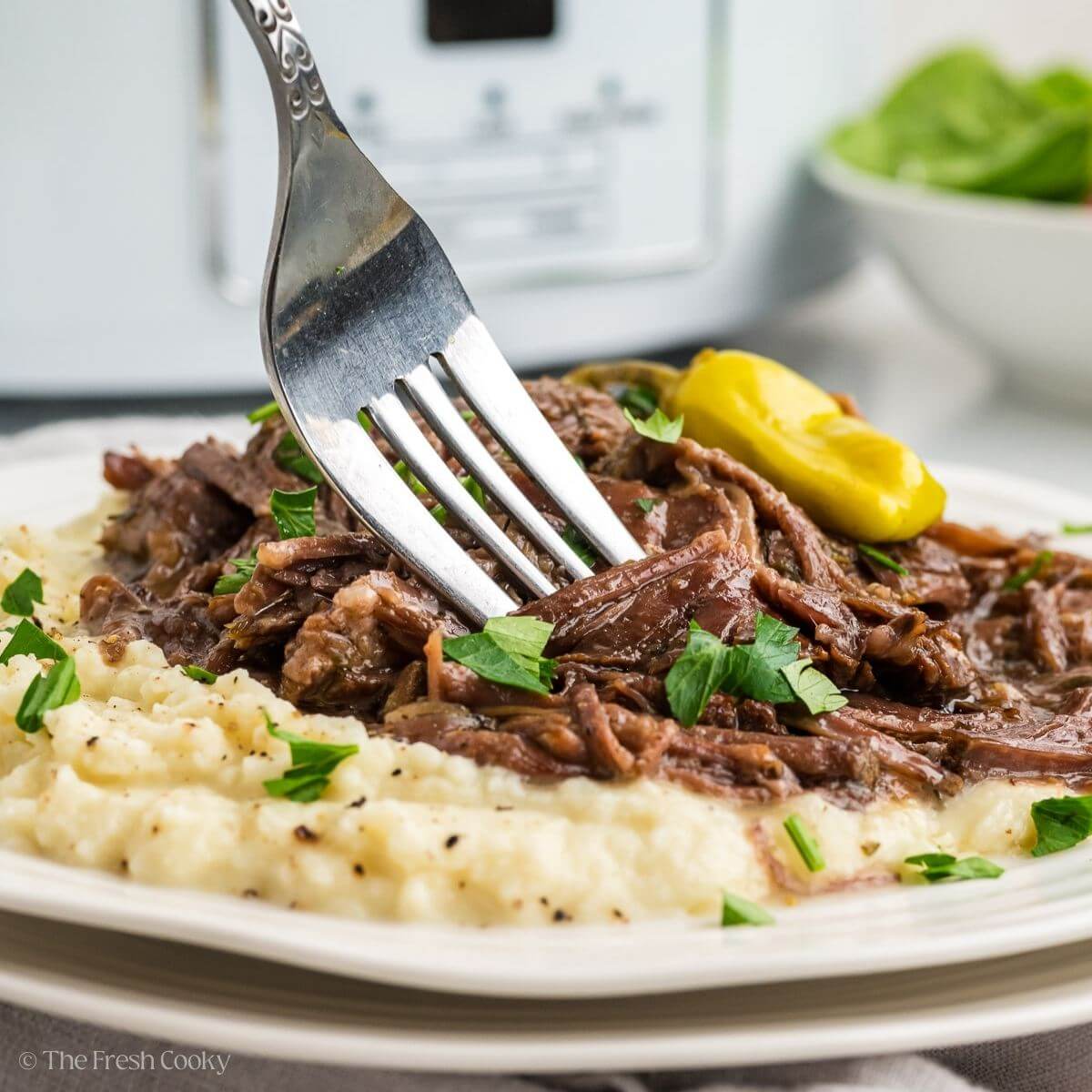 Fork being dipped into the shredded beef sitting on a bed of masted potatoes.