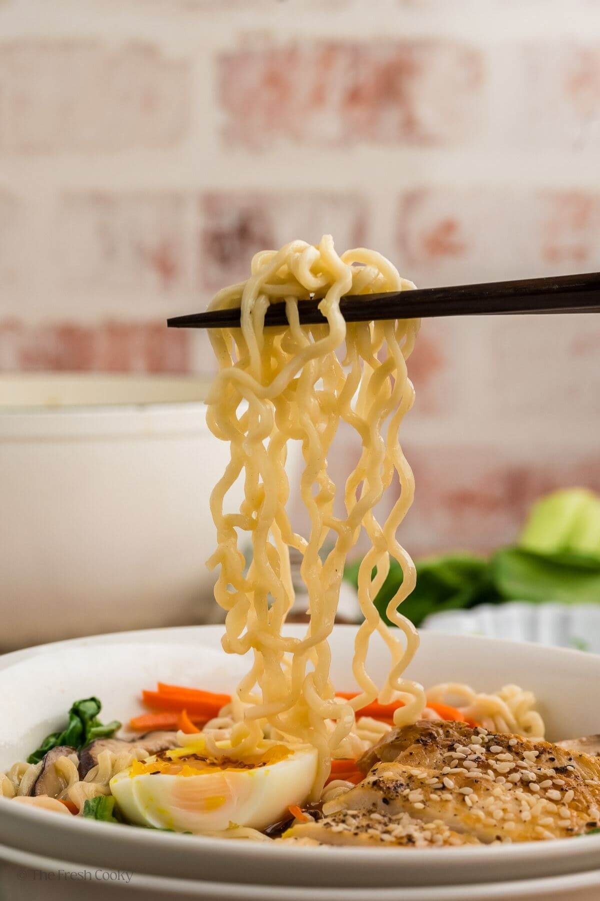 Chopsticks picking up ramen noodles from a bowl of ramen.