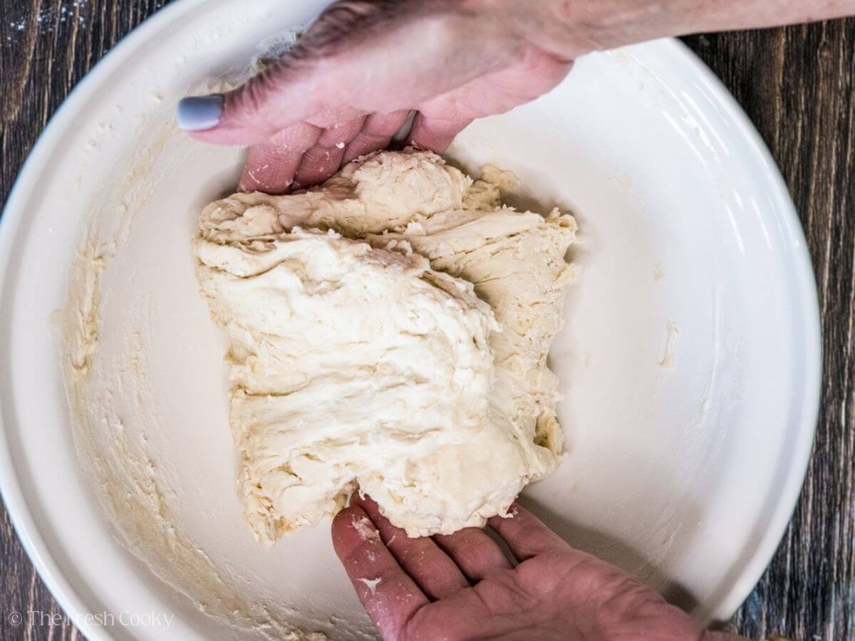 Two hands kneading the shaggy sourdough bread dough.