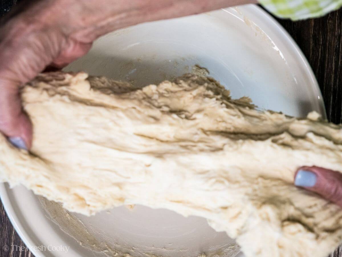 Two hands stretching out the sourdough bread dough.