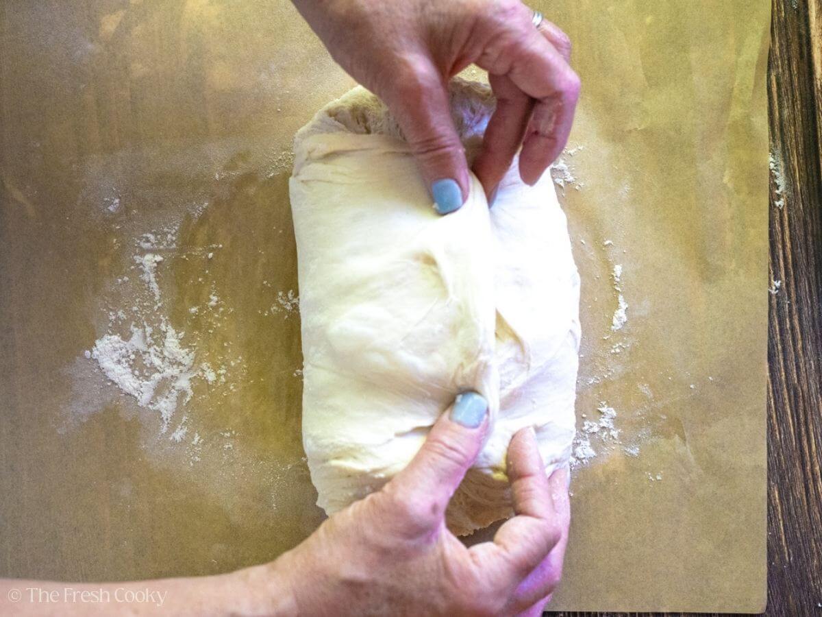 Two hands folding up the sourdough bread dough on a floured surface.
