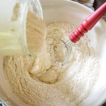 Using a bread spatula to mix together flour and sourdough starter.