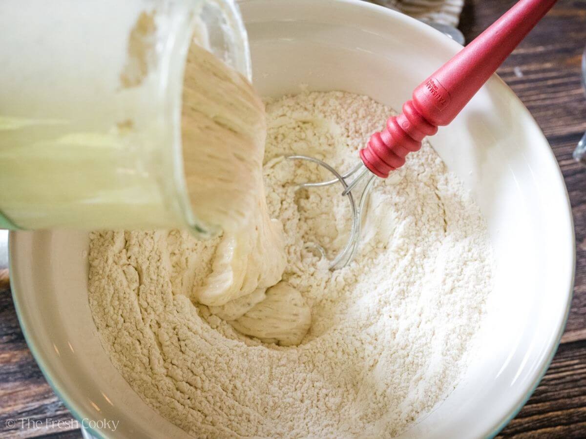 Using a bread spatula to mix together flour and sourdough starter.
