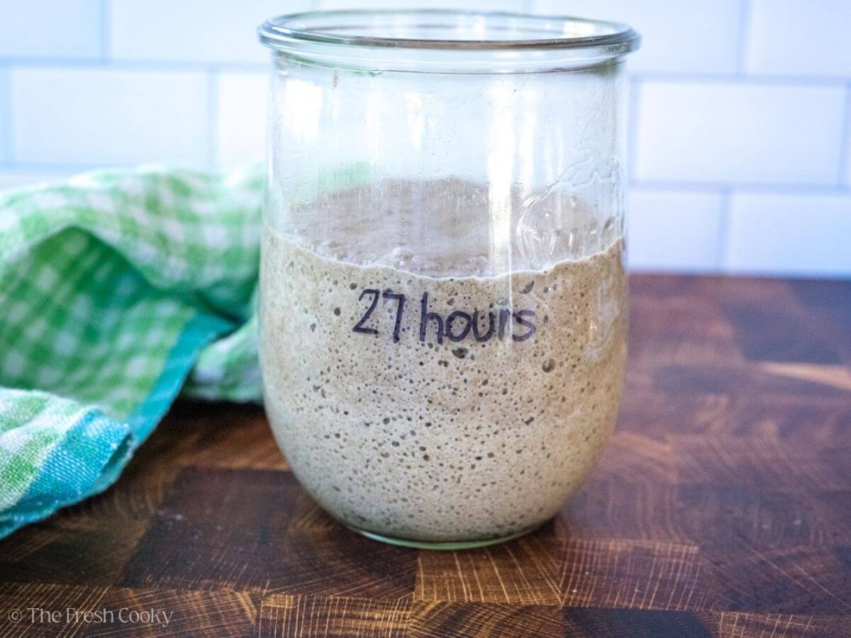 Glass jar of sourdough starter labeled "27 hours".