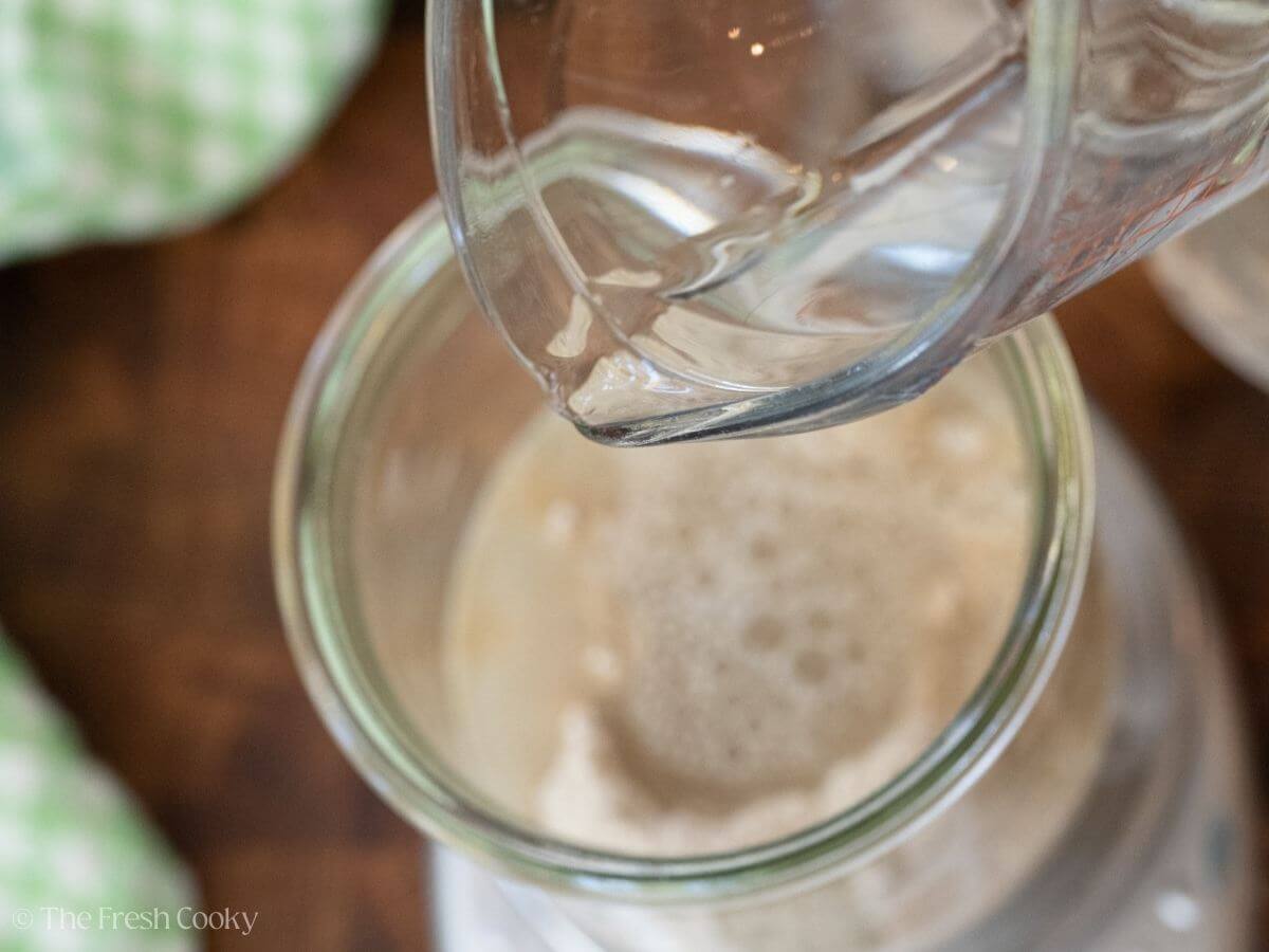Pouring water into the flour in a glass jar.