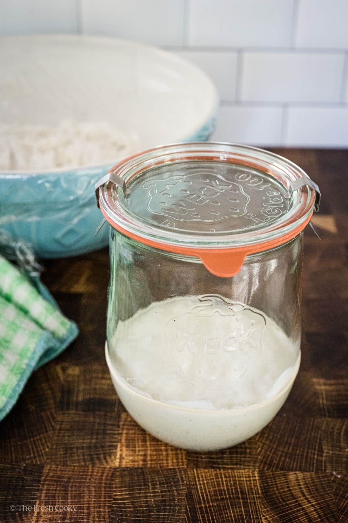 A jar of starter ready to go back into the fridge with bread starting behind.