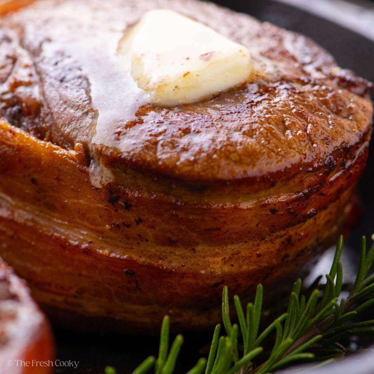 Close up shot of bacon wrapped filet mignon with a piece of butter melting on the top.