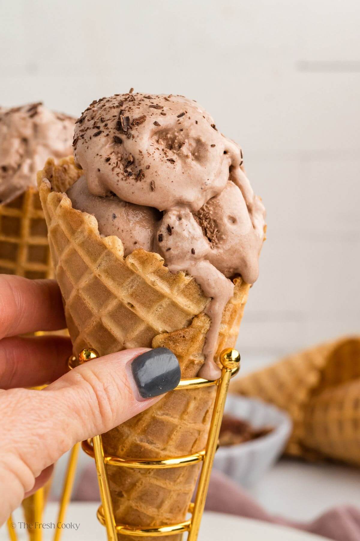 Hand holding cone with scoops of chocolate ice cream. 