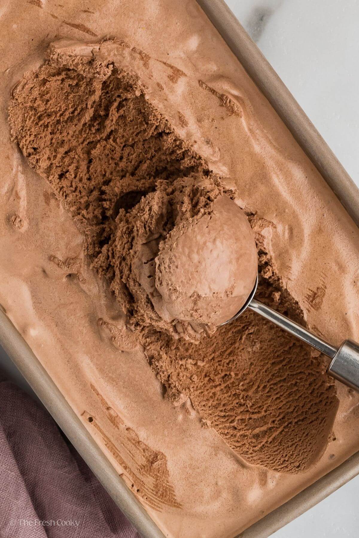 Close up of container of chocolate ice cream with ice cream scoop. 