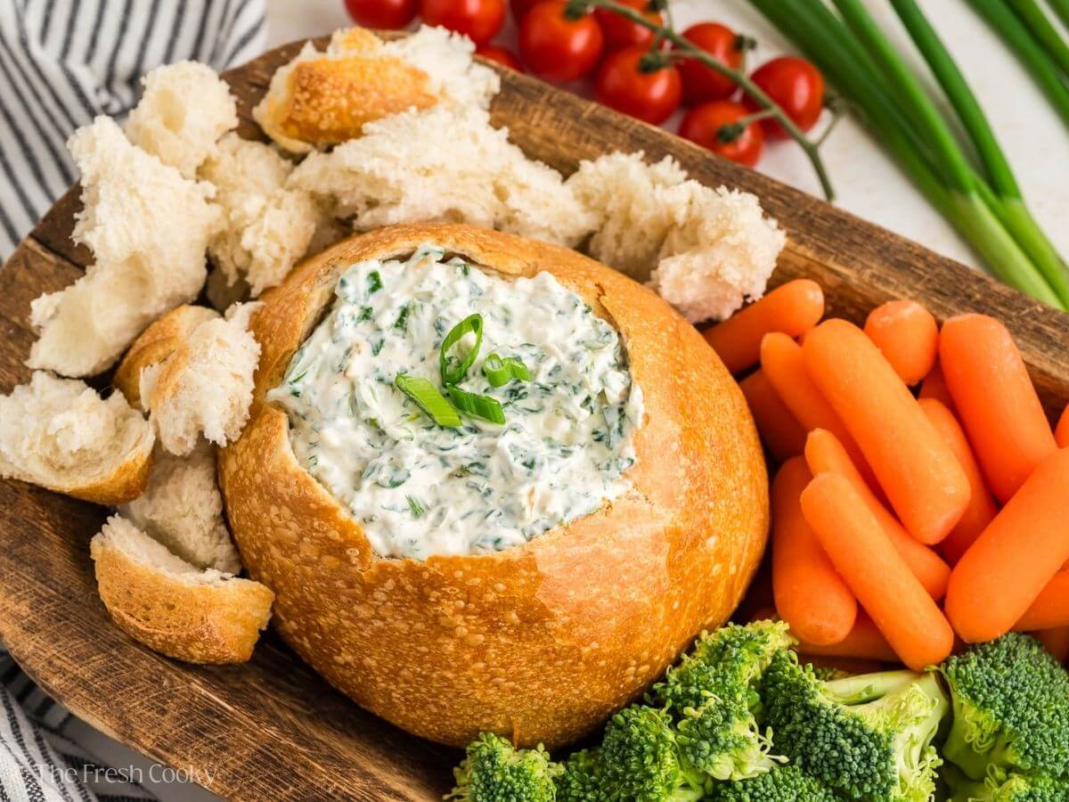 Knorr veggie spinach dip served in a bread bowl next to pieces of bread with carrots and broccoli.