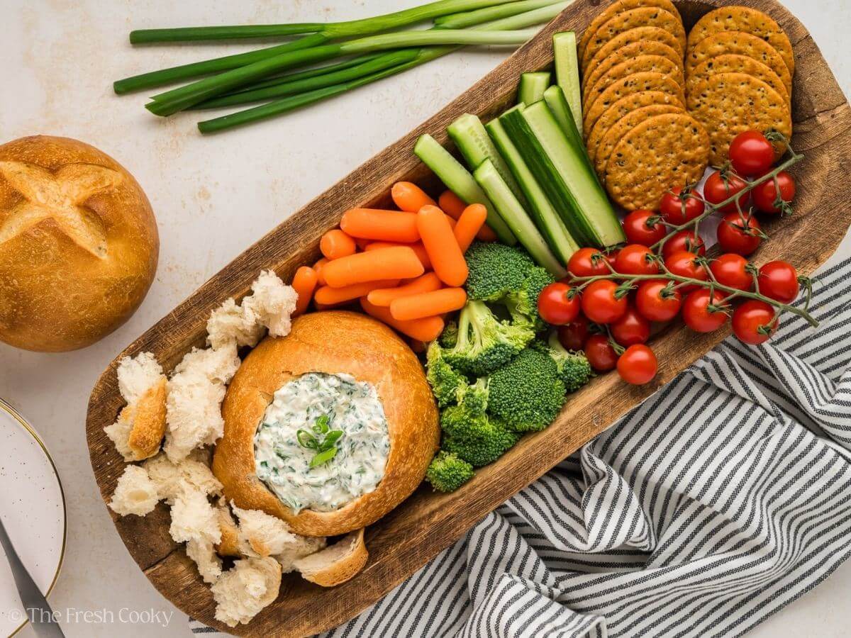Spinach dip in a bread bowl served with a spread of veggies, crackers and bread.