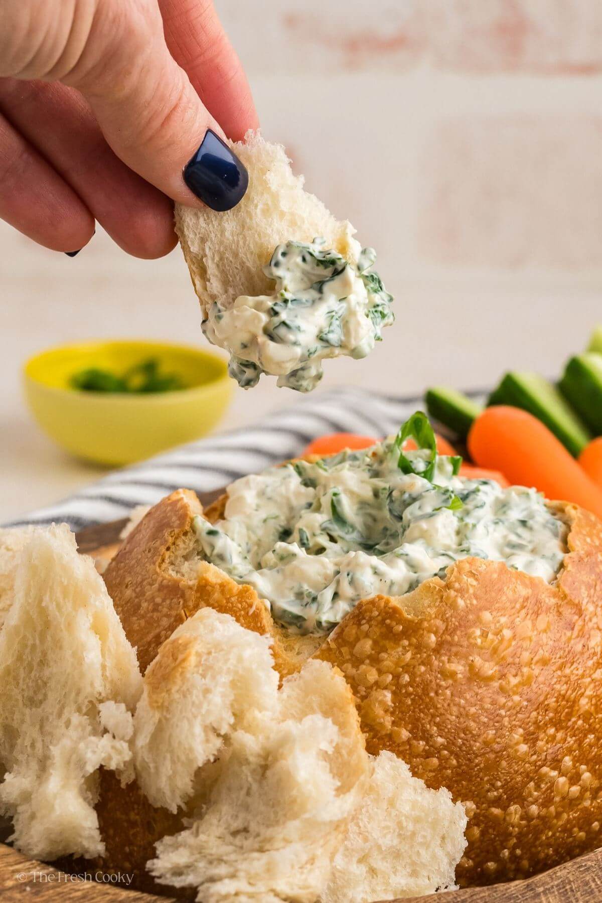 Hand dipping a piece of bread into the Knorr spinach dip in a bread bowl.