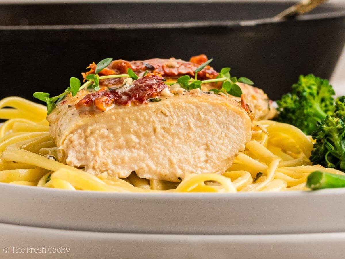 Side view of juicy chicken breast served on a bed of pasta with broccolini on the side.