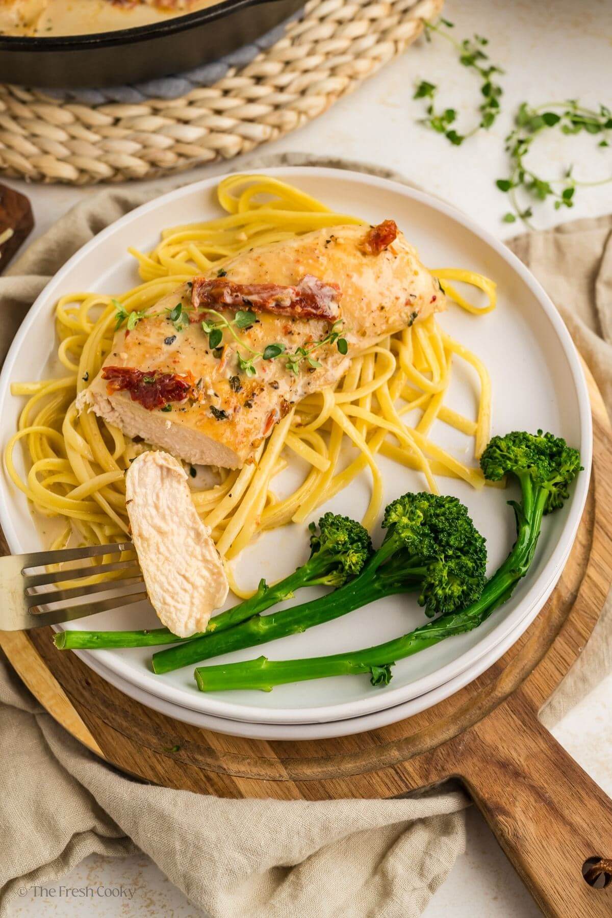 Plate with pasta, marry me chicken, and broccoli with a fork taking a piece of the chicken off.