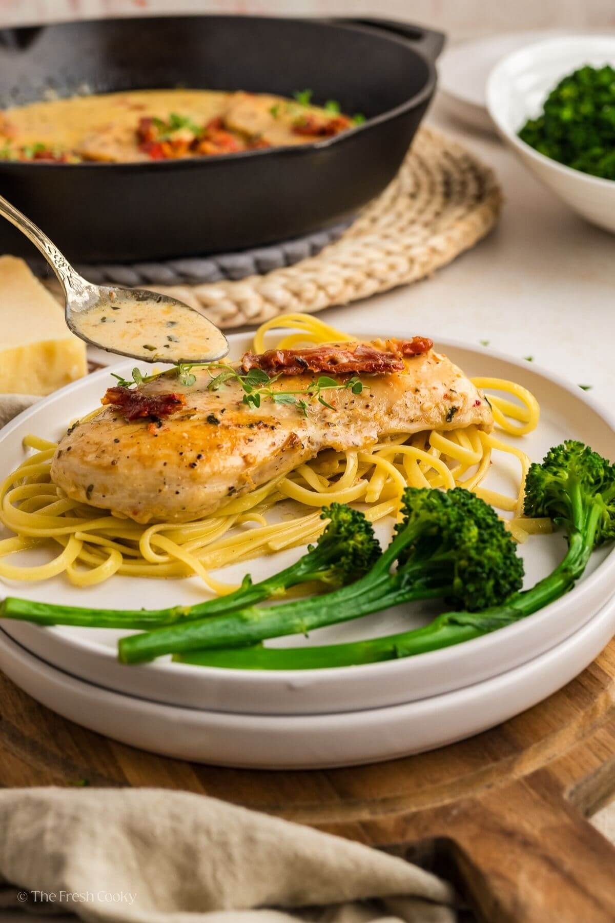 Spooning the marry me chicken sauce over the chicken breast on a bed of pasta on a plate.