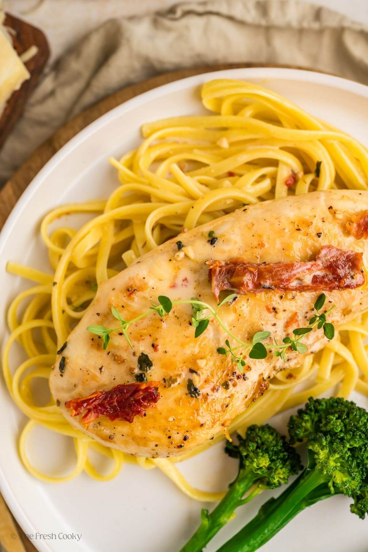 Overhead shot of a chicken breast on a bed of pasta with sauce on top on a white plate.