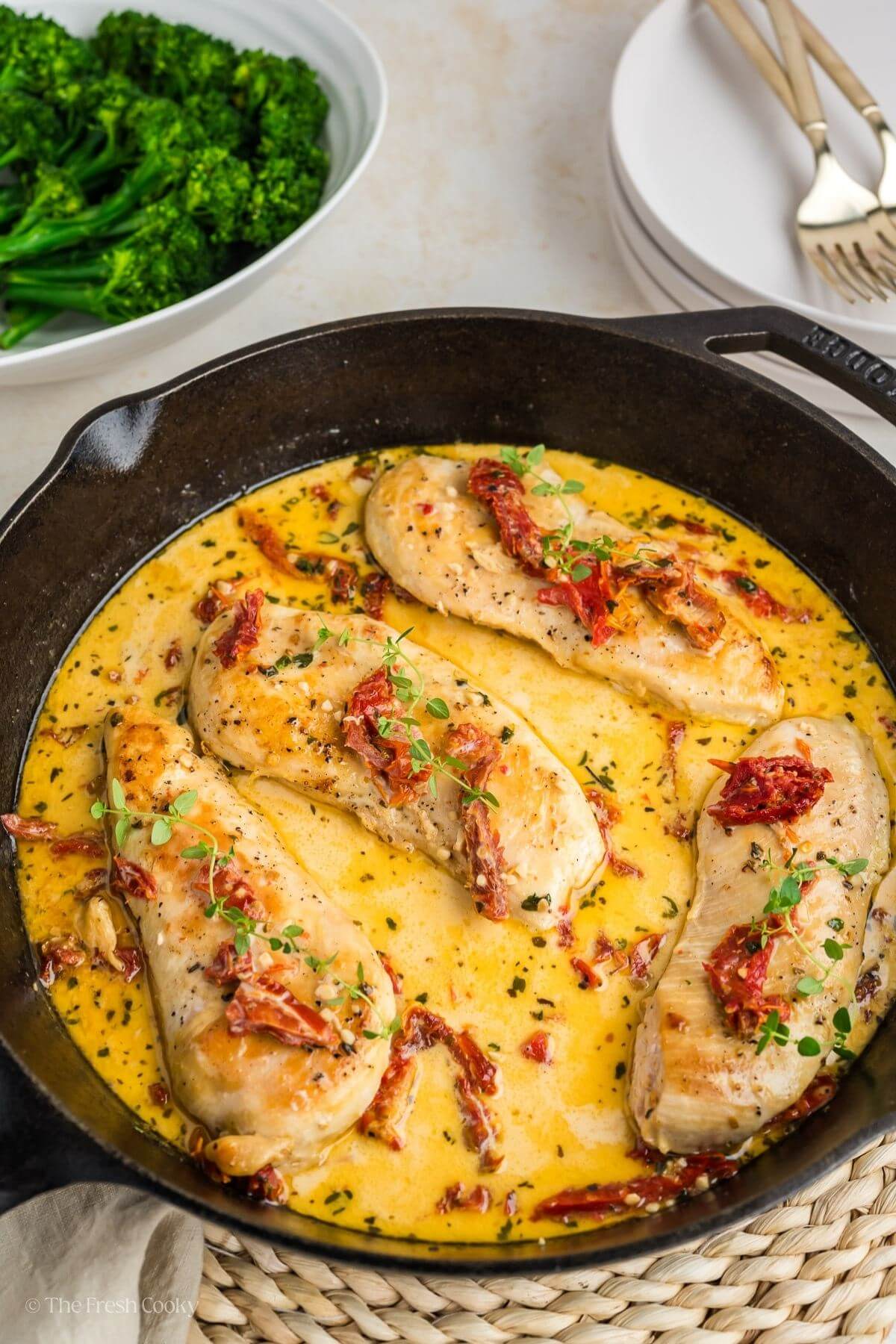 Four chicken breasts in a creamy sauce with sun-dried tomatoes in a cast iron skillet.