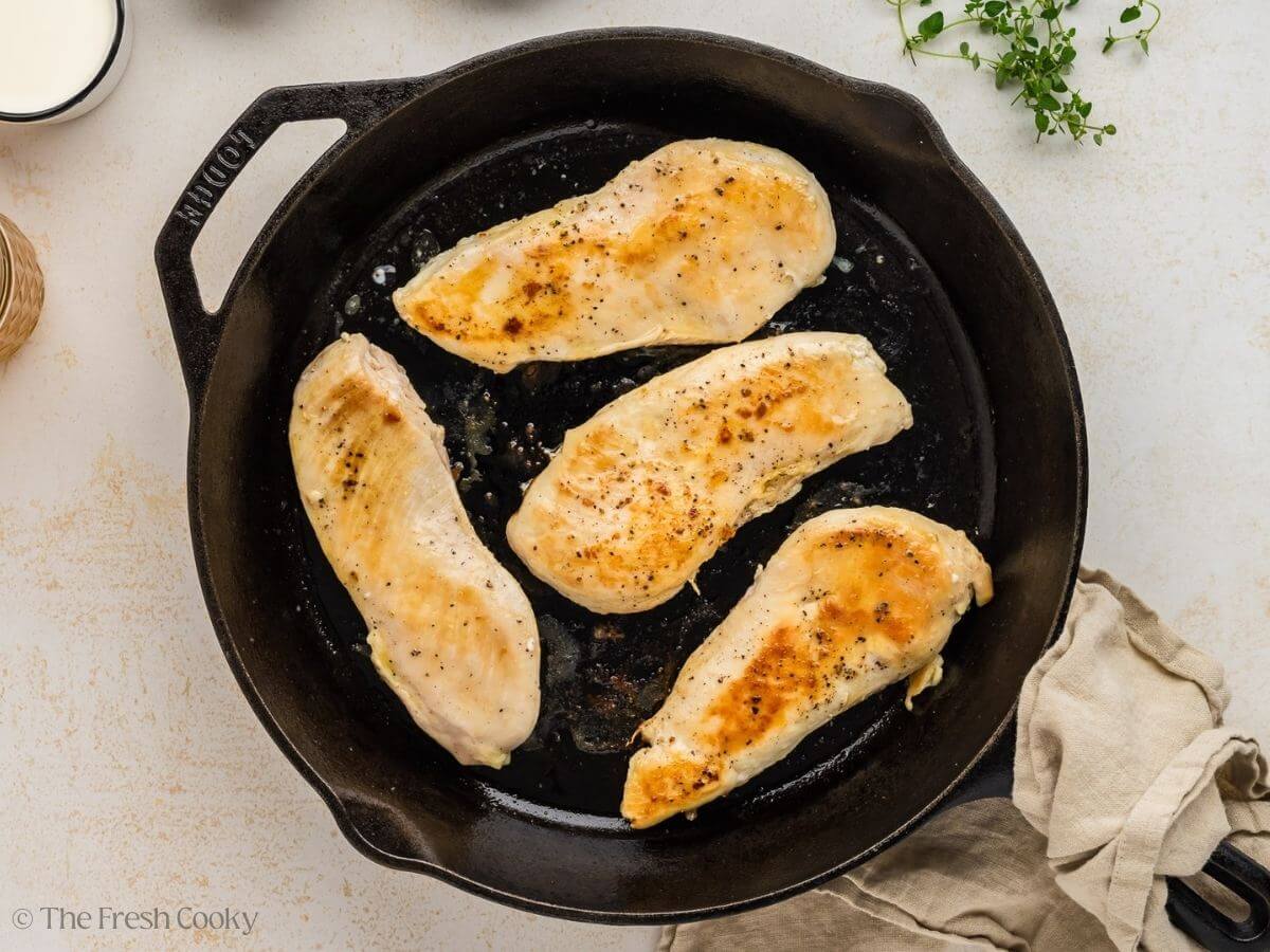 Chicken breast being seared in a cast iron skillet.