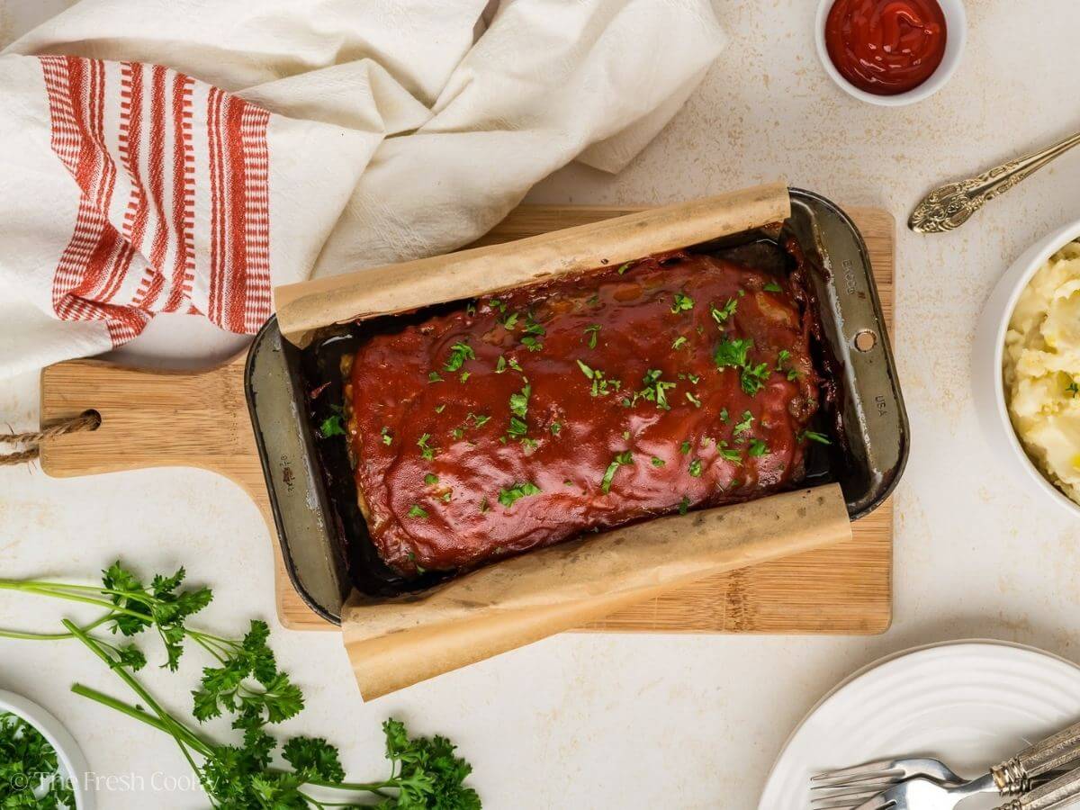 Meatloaf in a loaf pan topped with fresh parsley.