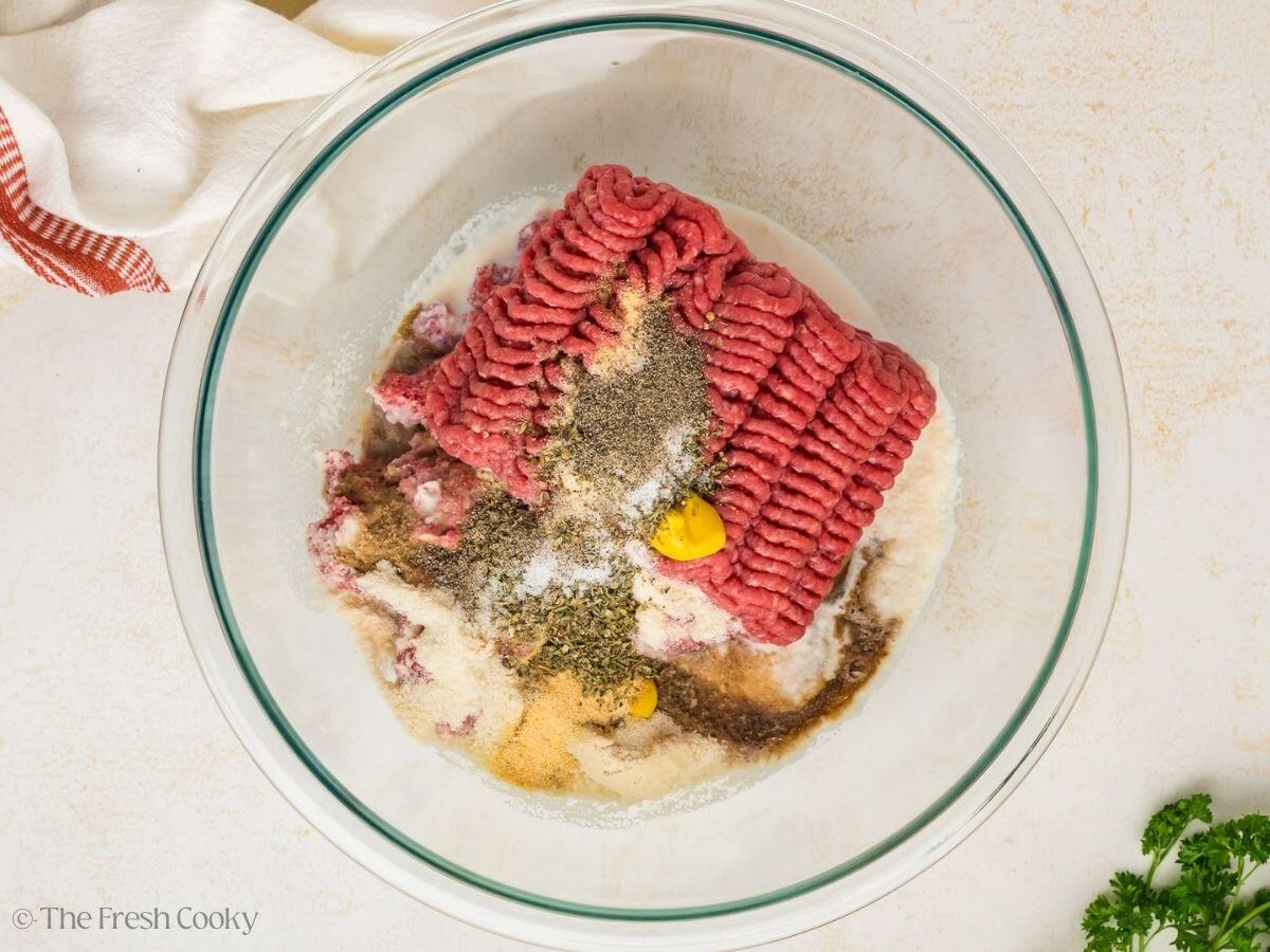 Meatloaf ingredients in a glass mixing bowl before being mixed together.