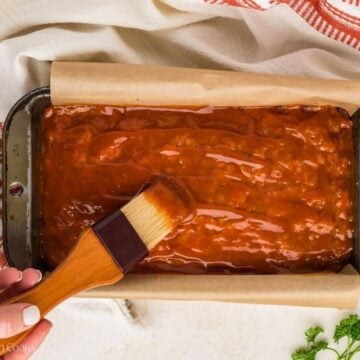 Brushing the glaze on top of the meatloaf before baking it.