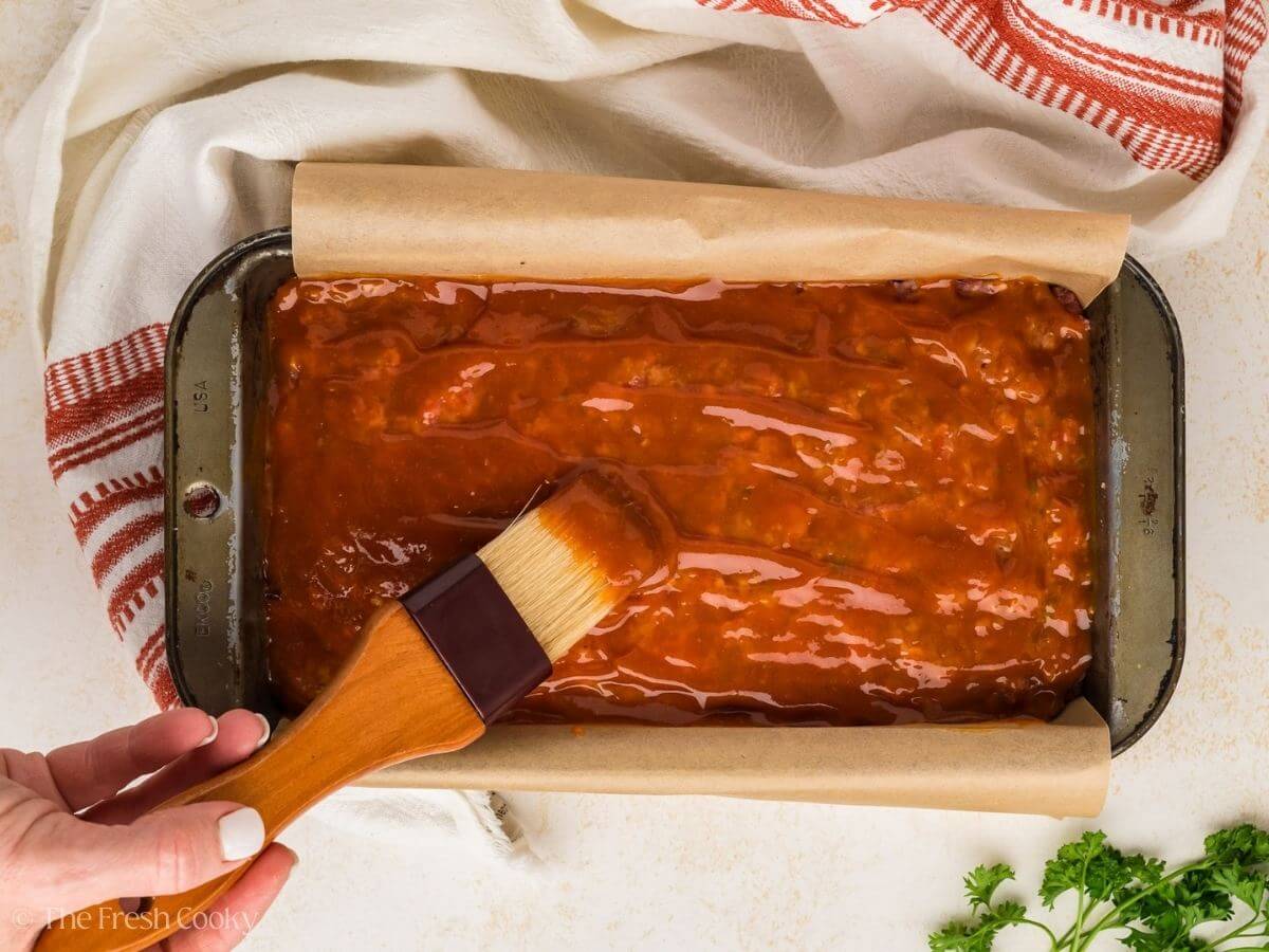 Brushing the glaze on top of the meatloaf before baking it.
