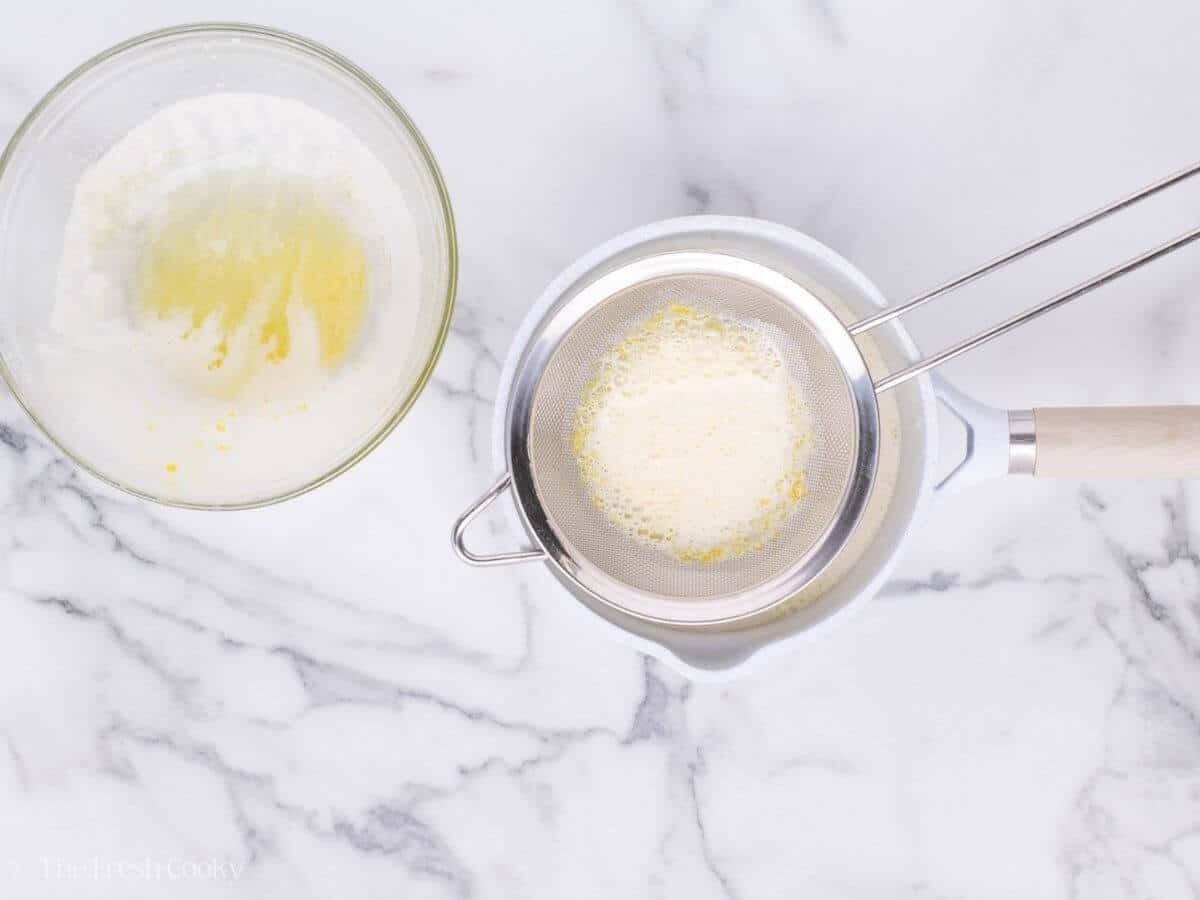 Pouring the egg yolk and cream mixture over a fine mesh sieve.
