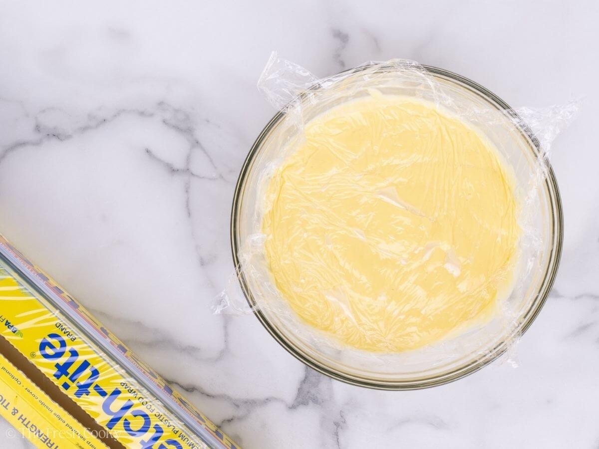 Custard in a glass mixing bowl with a piece of plastic wrap on top.