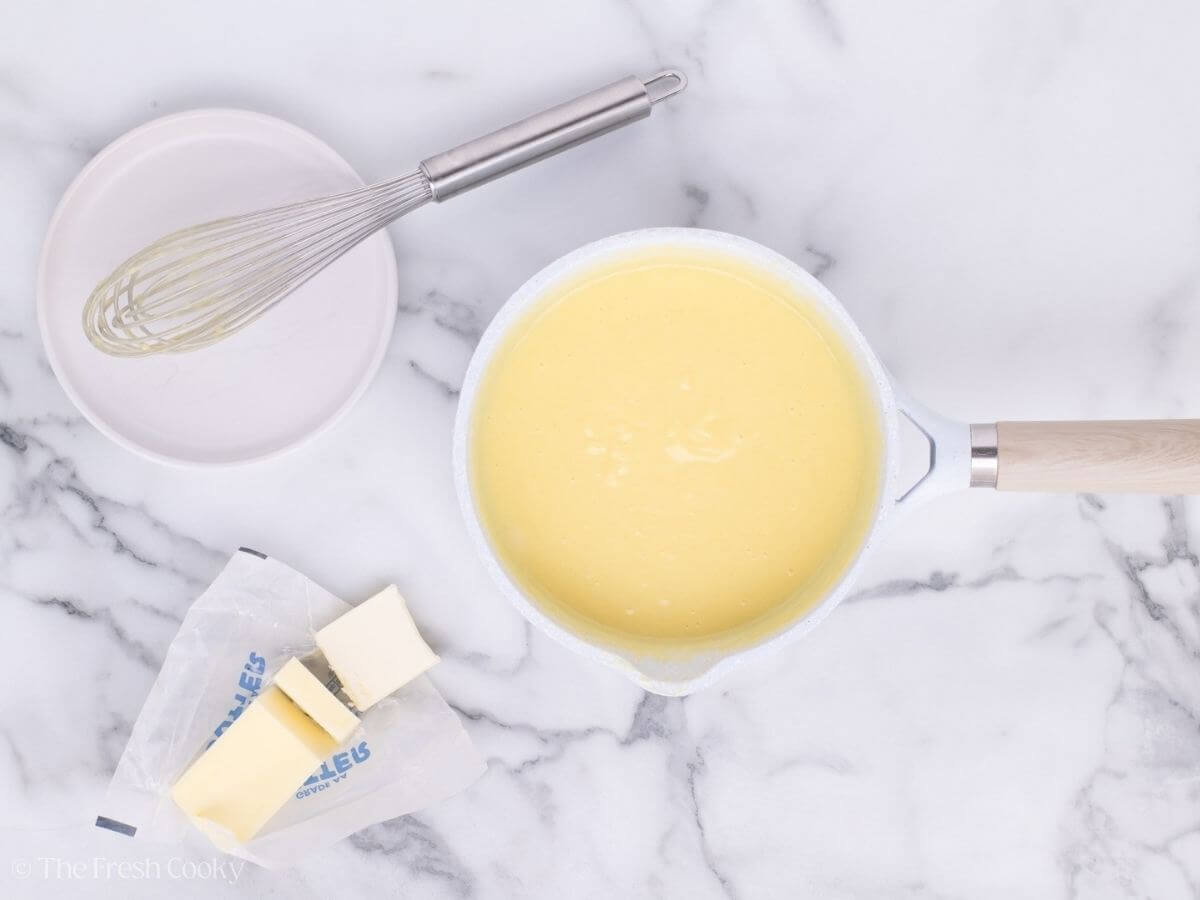 Warm custard in a saucepan next to some slices of butter.