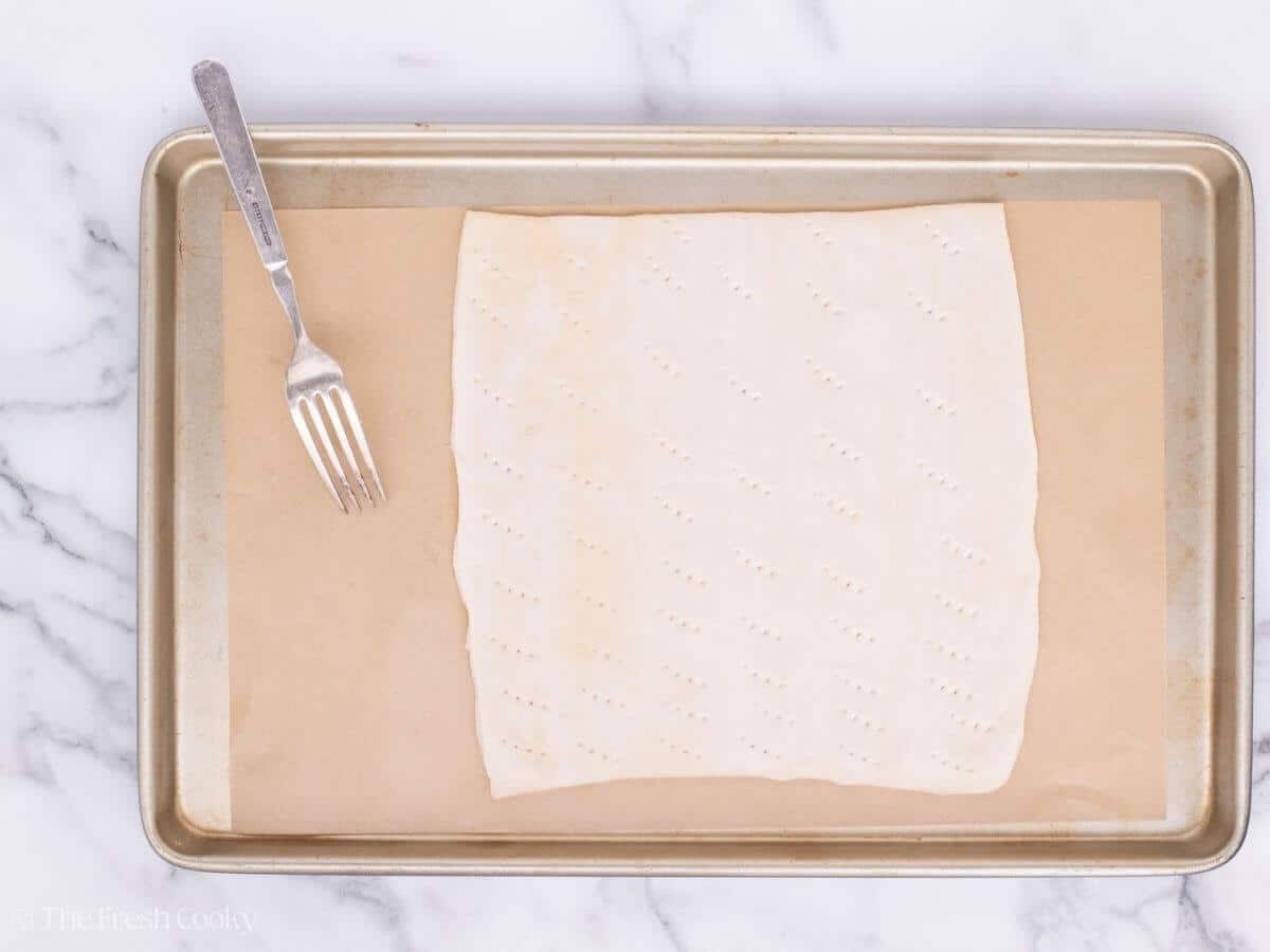 Puff pastry sheet on a sheet pan poked with a fork.