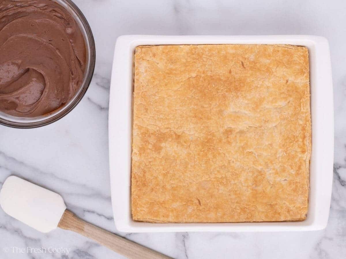 Puff pastry in a baking dish next to a bowl of chocolate ganache.
