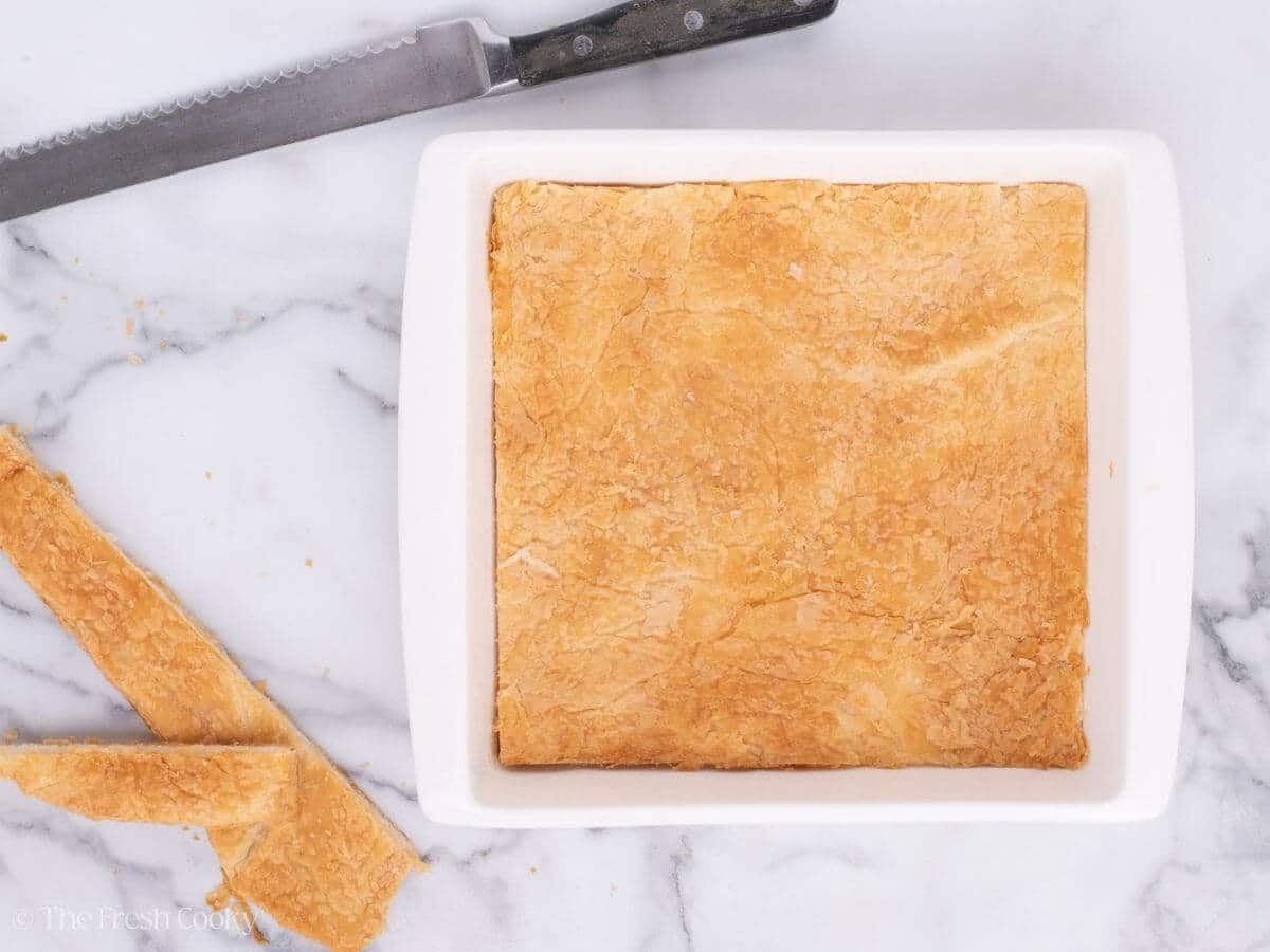 Baked puff pastry sheet placed in the bottom of a white baking dish.