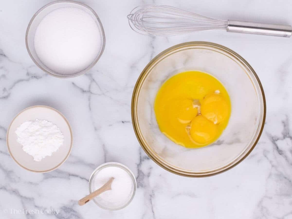 Egg yolks in a mixing bowl next to sugar, cornstarch, and salt.