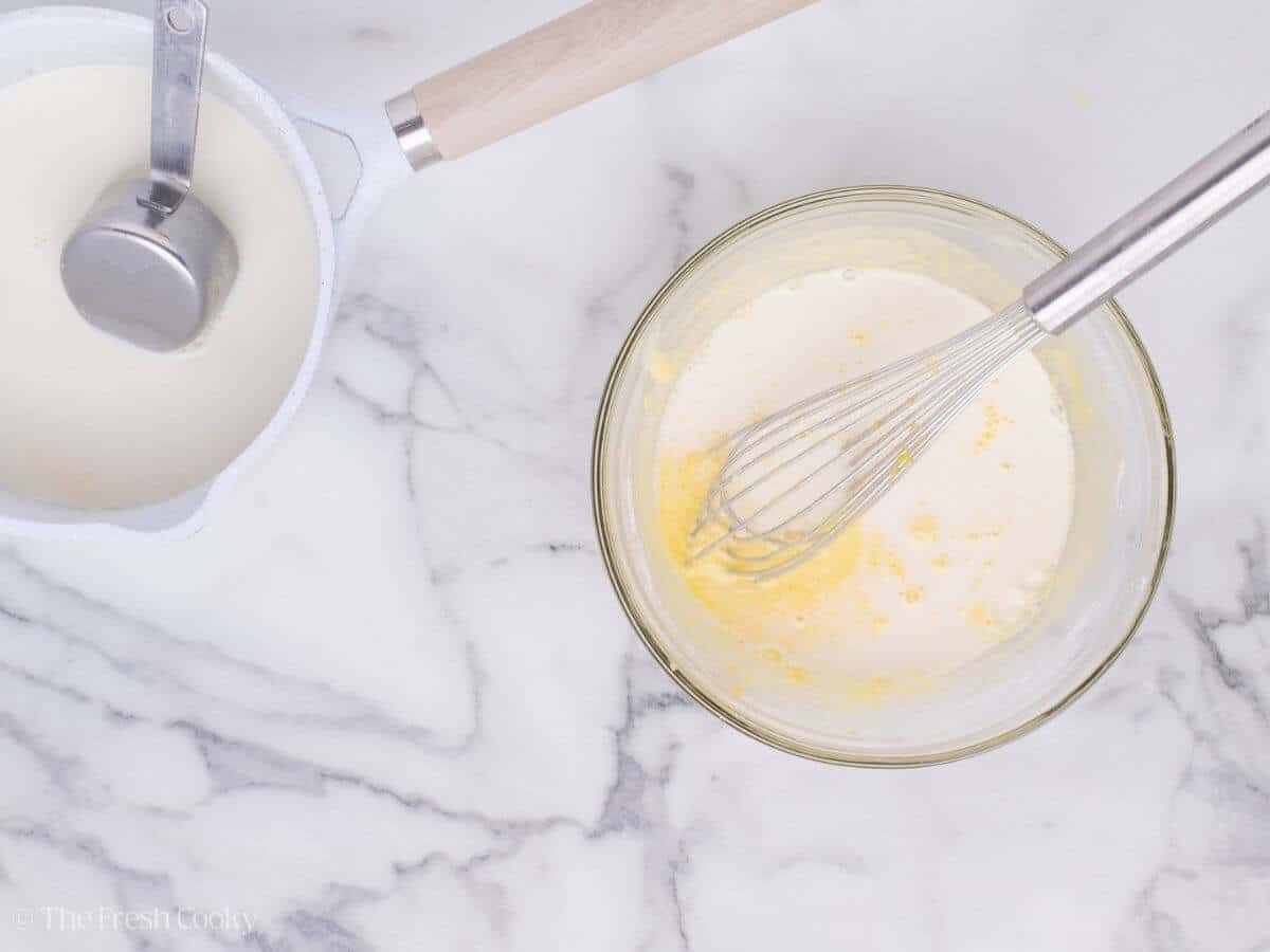 Warm milk being gently whisked into the egg yolk mixture.