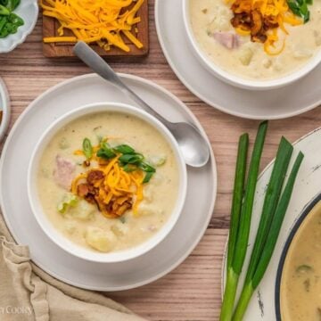 Table filled with two bowls of potato soup, a pot of soup, and the toppings on the side.