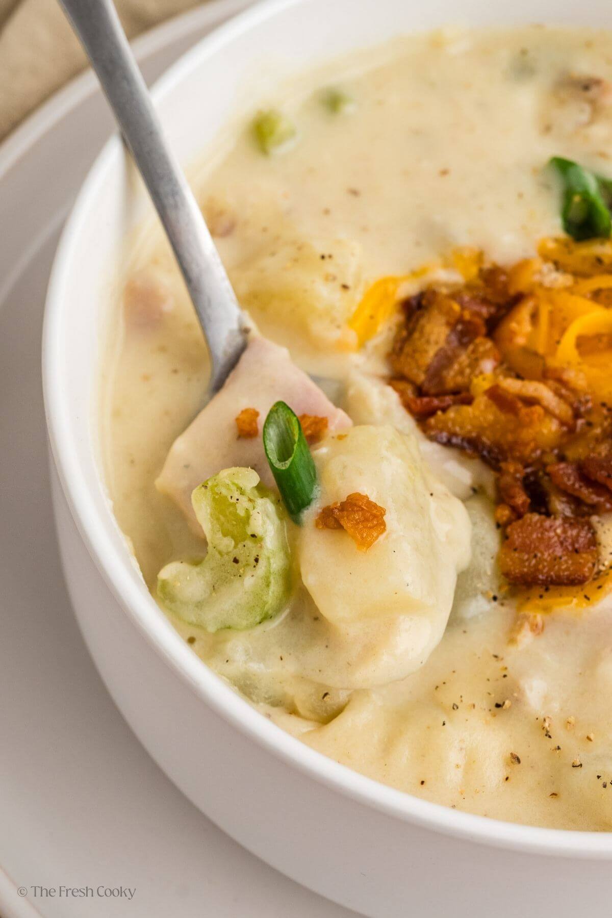 Ham and potato soup in a bowl with a spoon scooping up a bite.